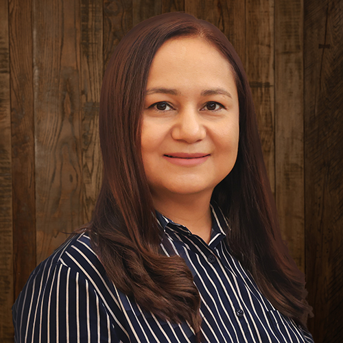 Portrait of a woman with long brown hair wearing a navy striped blouse, smiling against a wood-paneled background.
